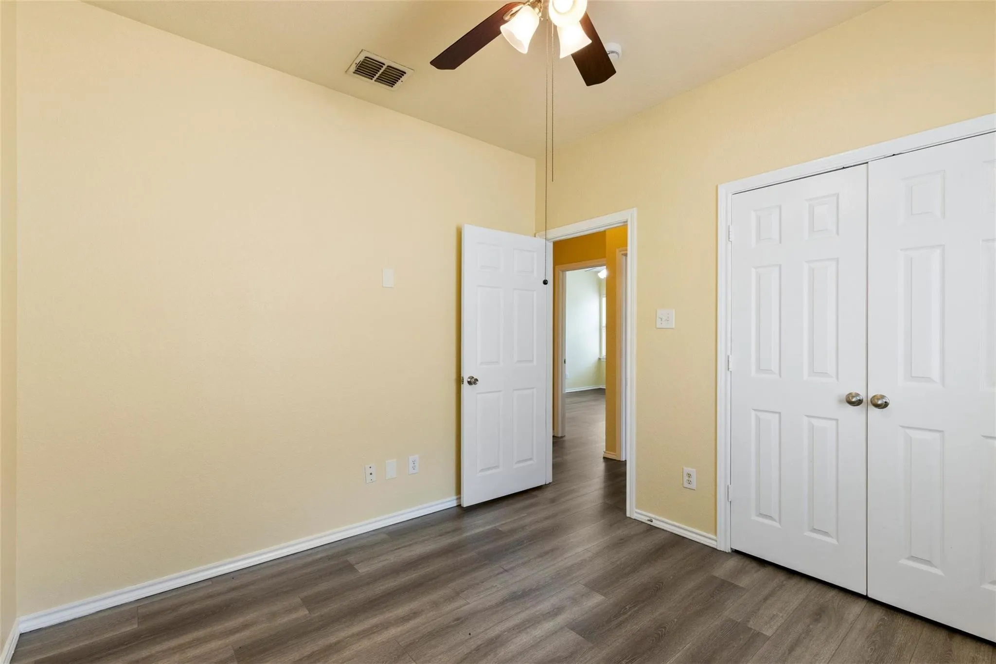 Wood-finish flooring throughout, white baseboards, and a ceiling fan with integrated lighting