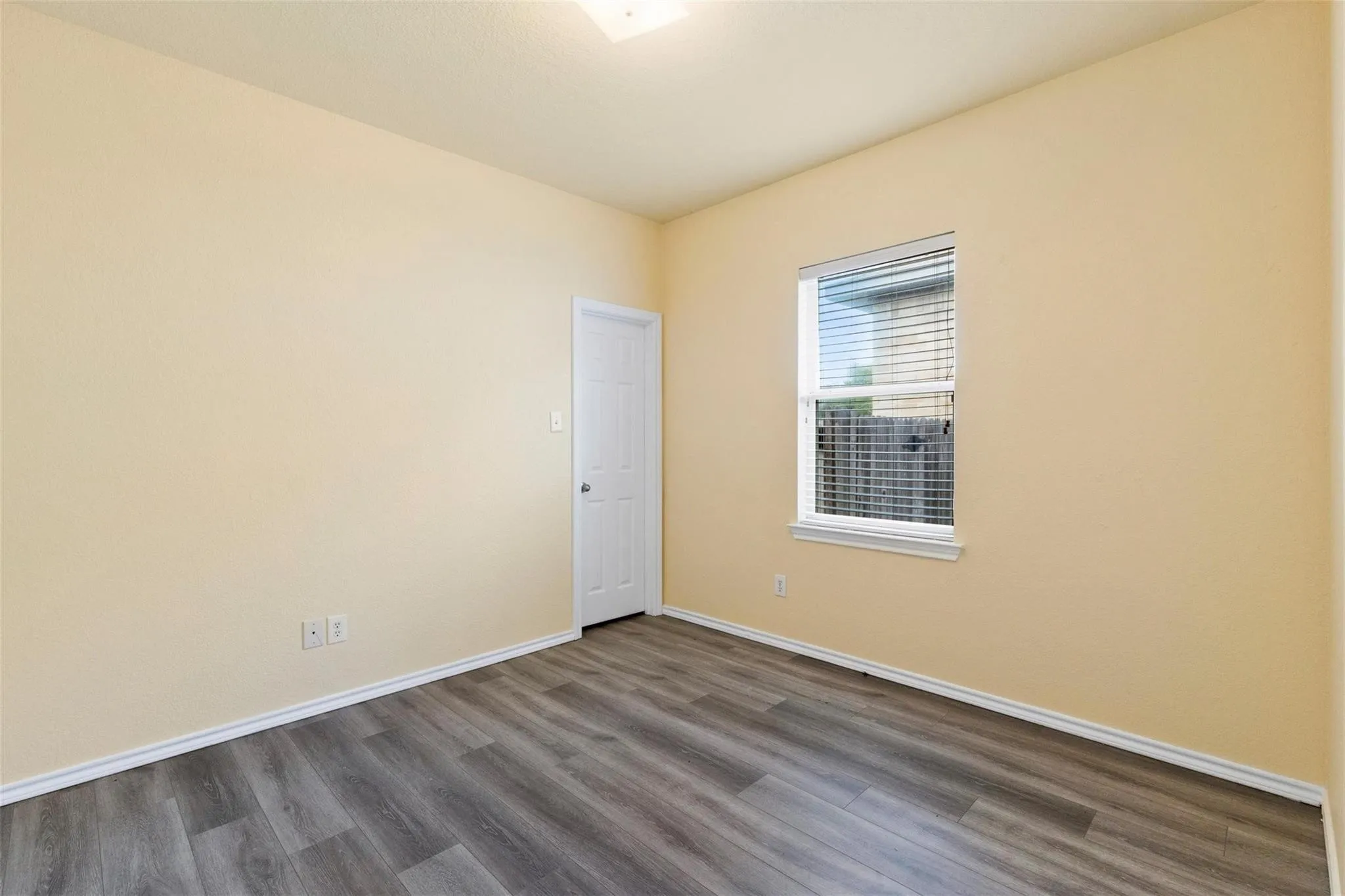 Wood-finish flooring, single window with blinds, and a paneled door