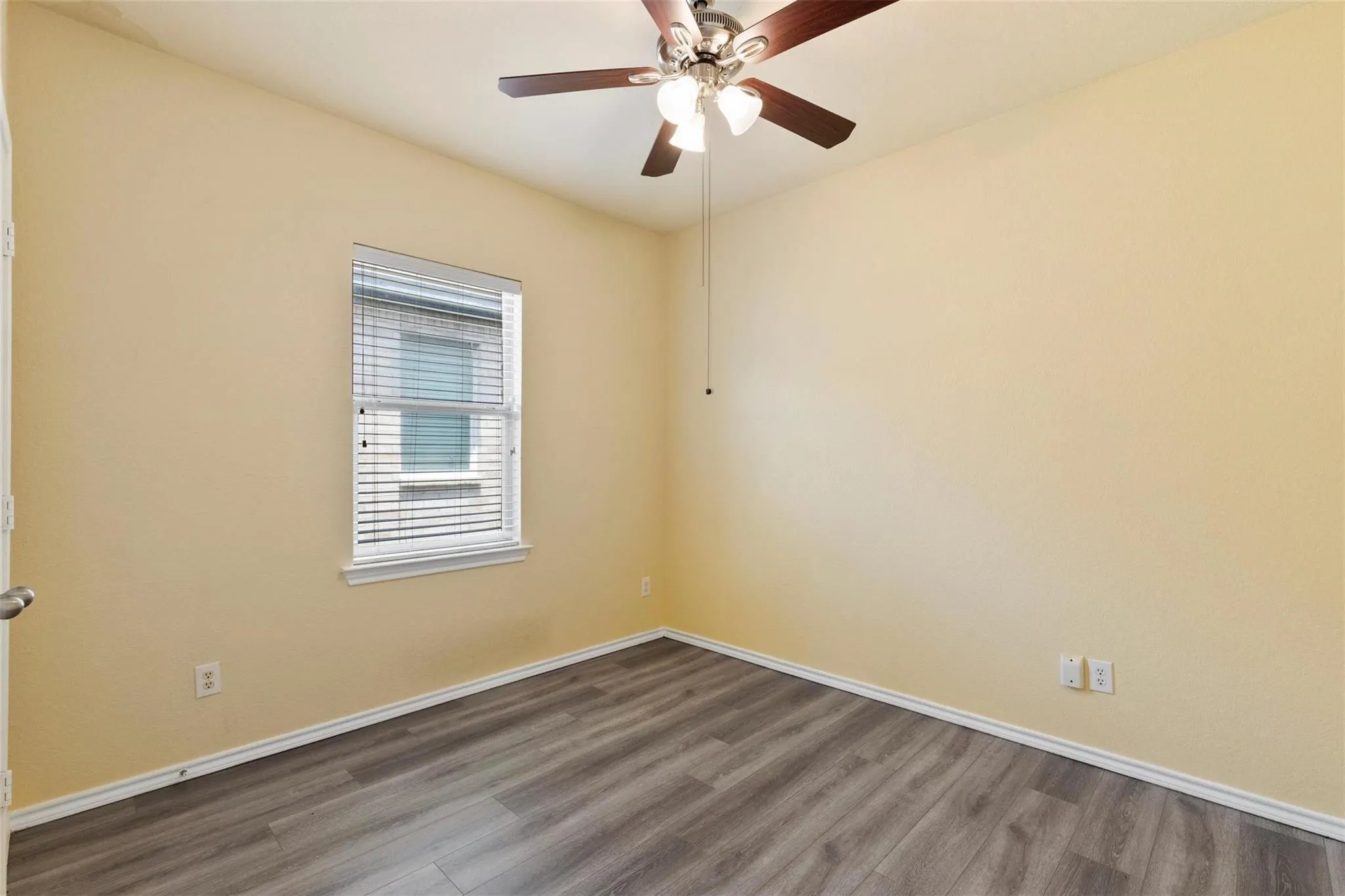 Wood-finish flooring, neutral wall color, window with blinds, and ceiling fan with integrated lighting