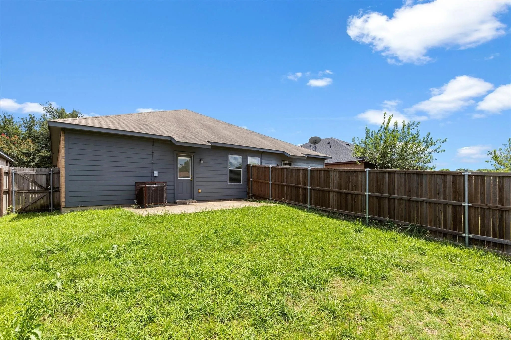 Expansive backyard featuring a privacy fence, concrete patio, and a side access gate