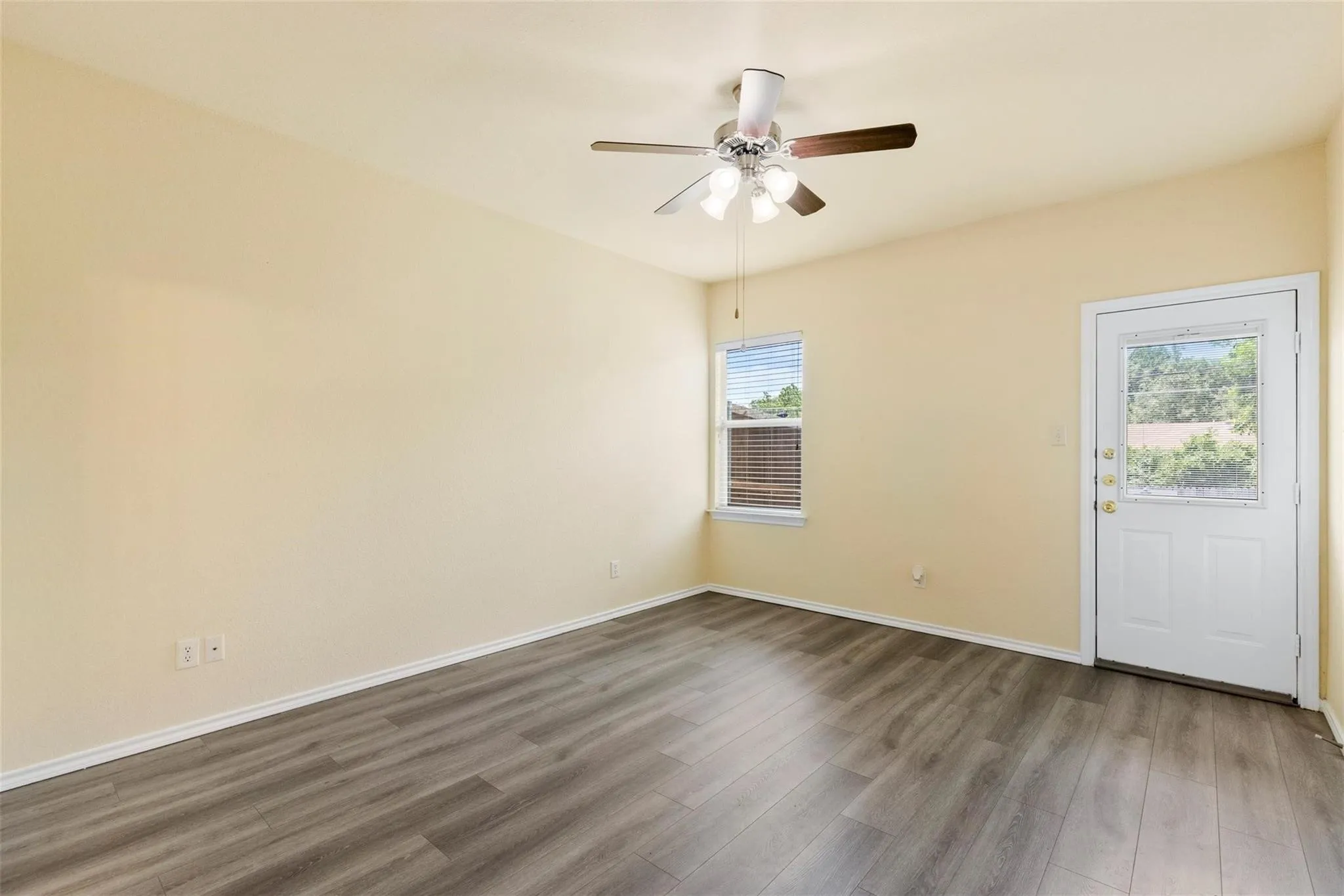 Wood-finish flooring, ceiling fan with integrated lighting, single window with horizontal blinds, and a white exterior door with glass paneling