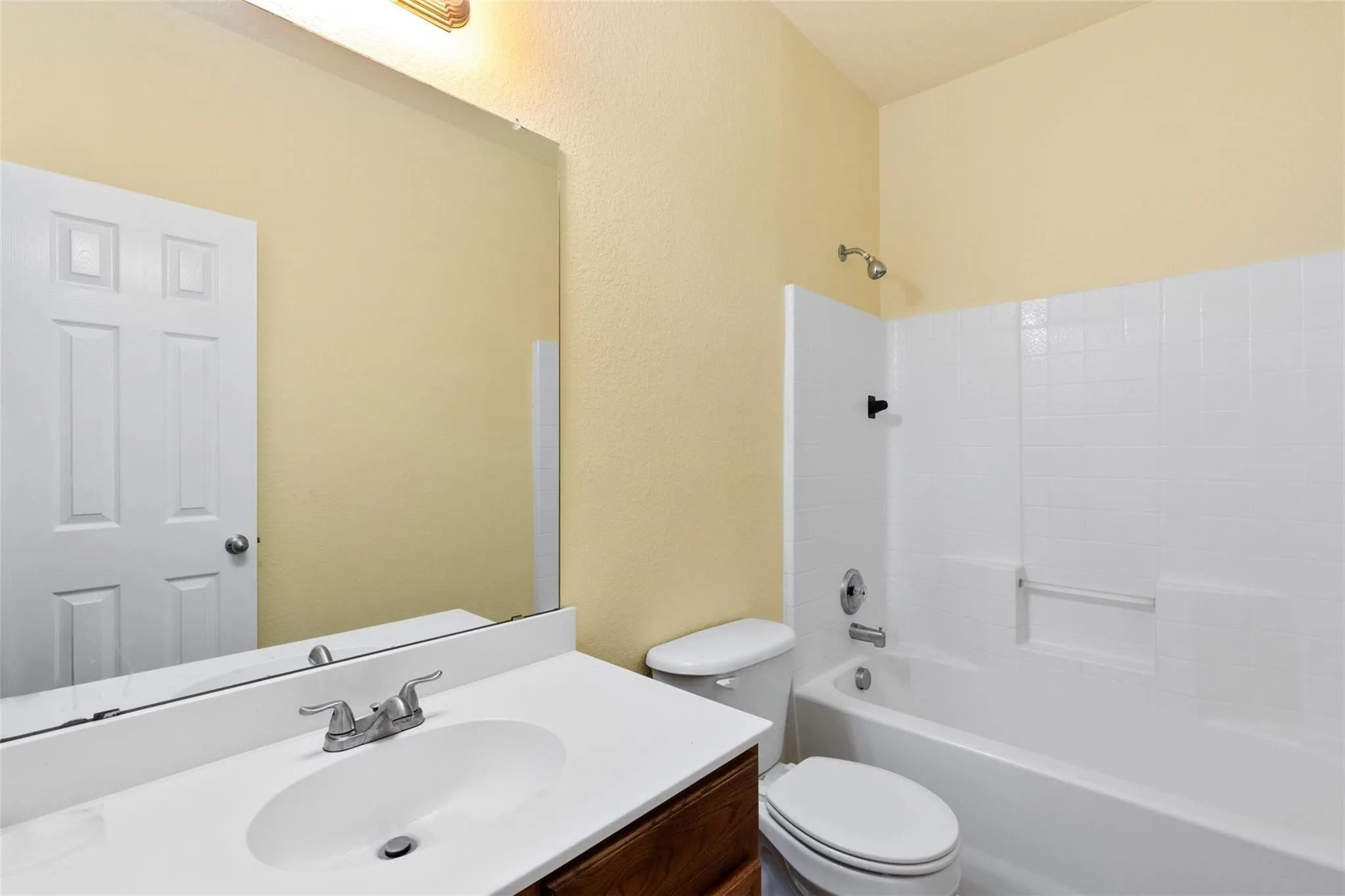 Bathroom featuring a white vanity with integrated sink, chrome faucet, wall-mounted mirror, and a combination tub/shower with white tile surround