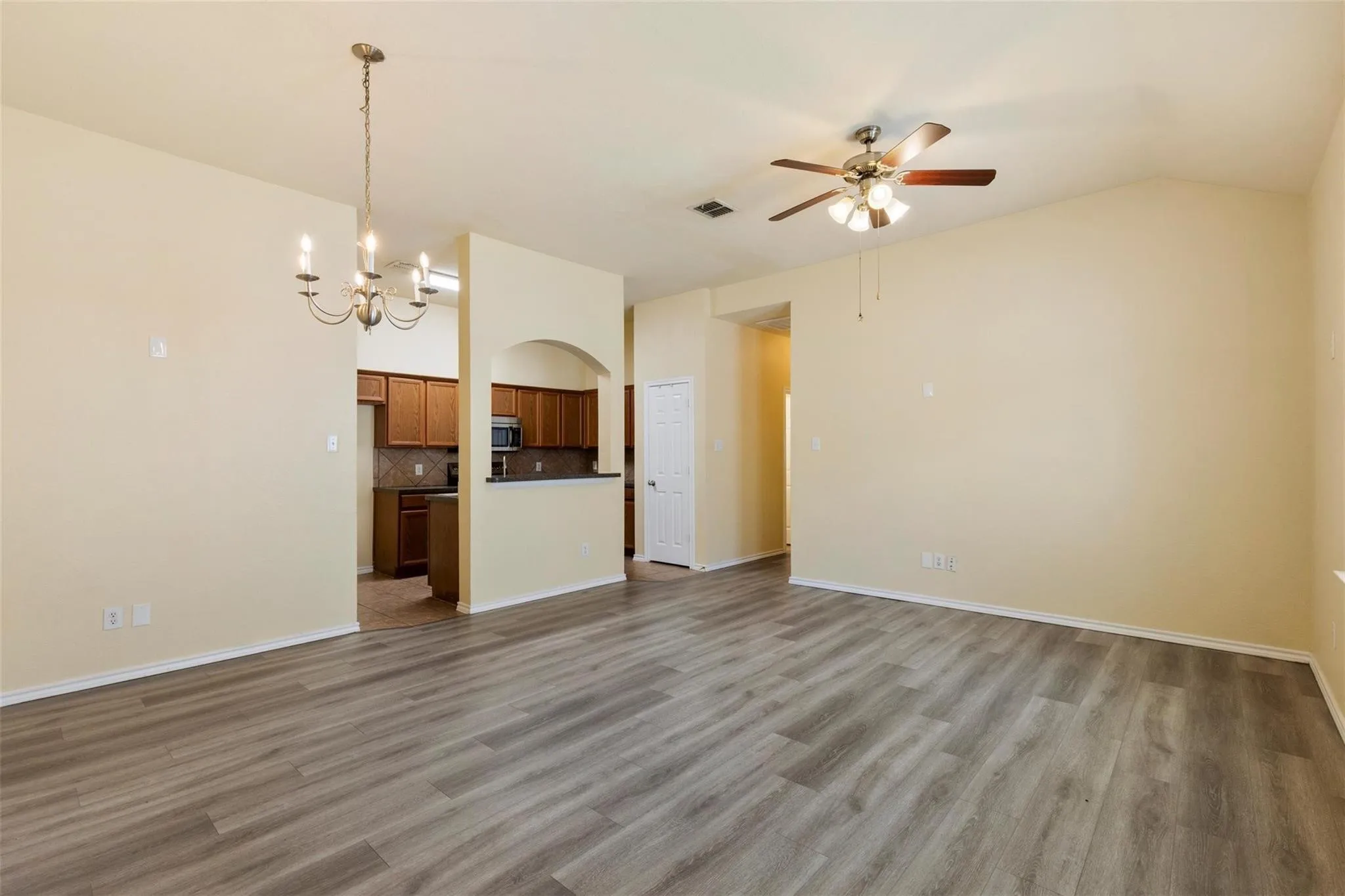 Vaulted ceiling with a ceiling fan, wood-finish flooring, and an arched kitchen passthrough