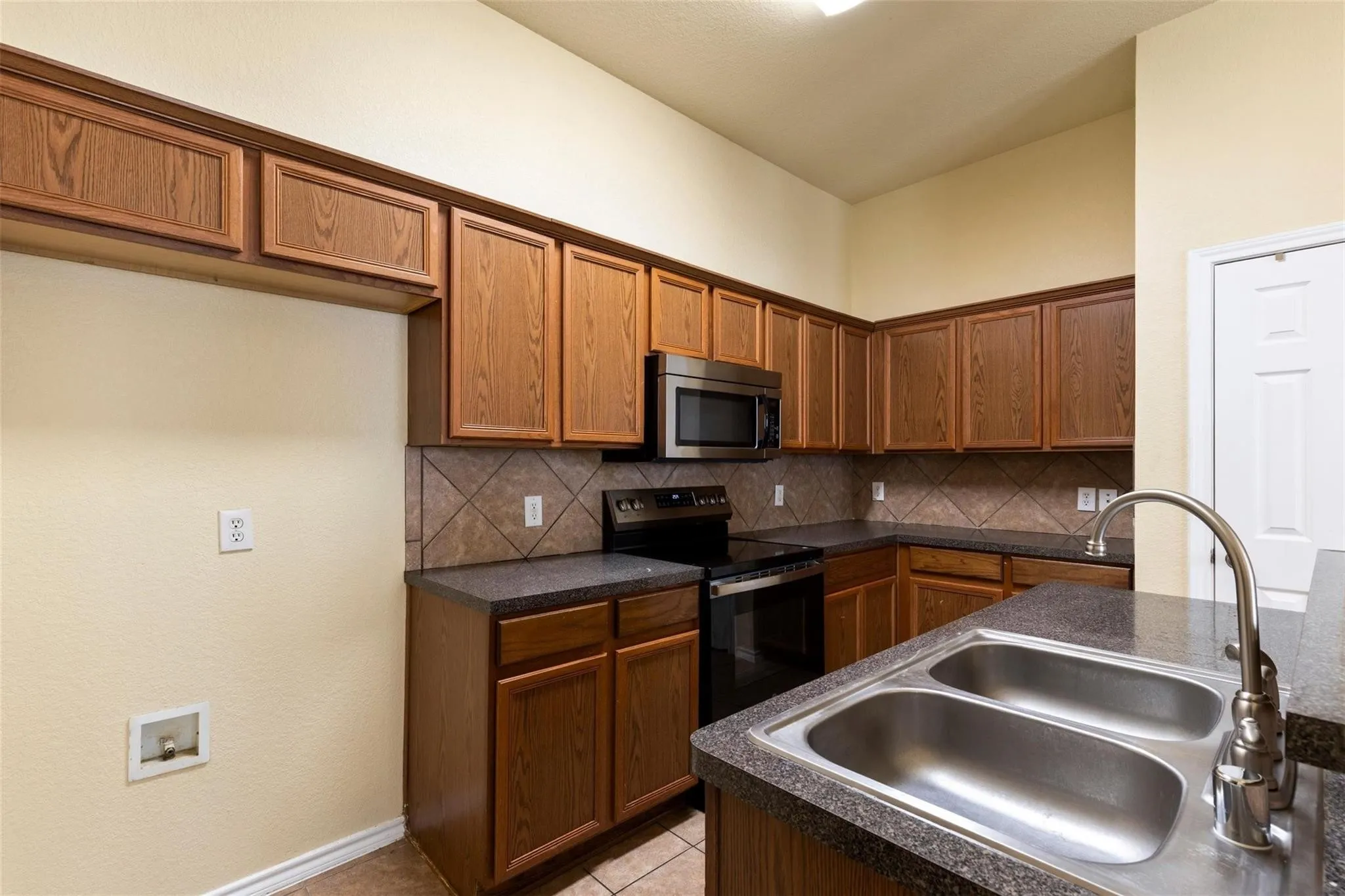 Kitchen featuring wood-finish cabinetry, stainless steel microwave, black electric range, and dark countertops