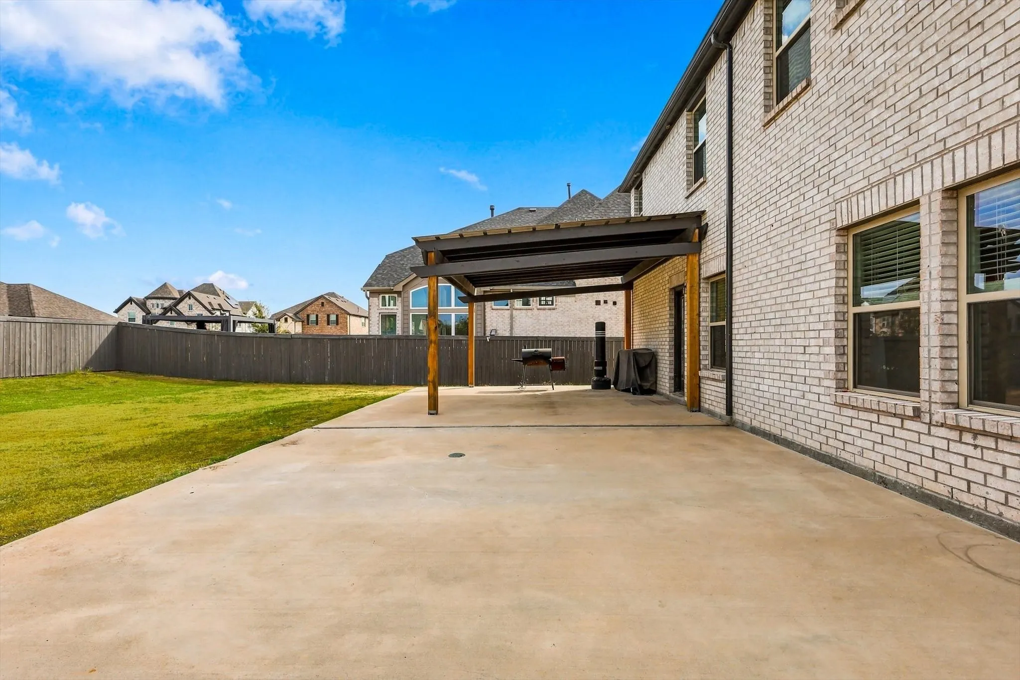 Expansive concrete patio with a modern pergola, complemented by a large green lawn and a full privacy fence
