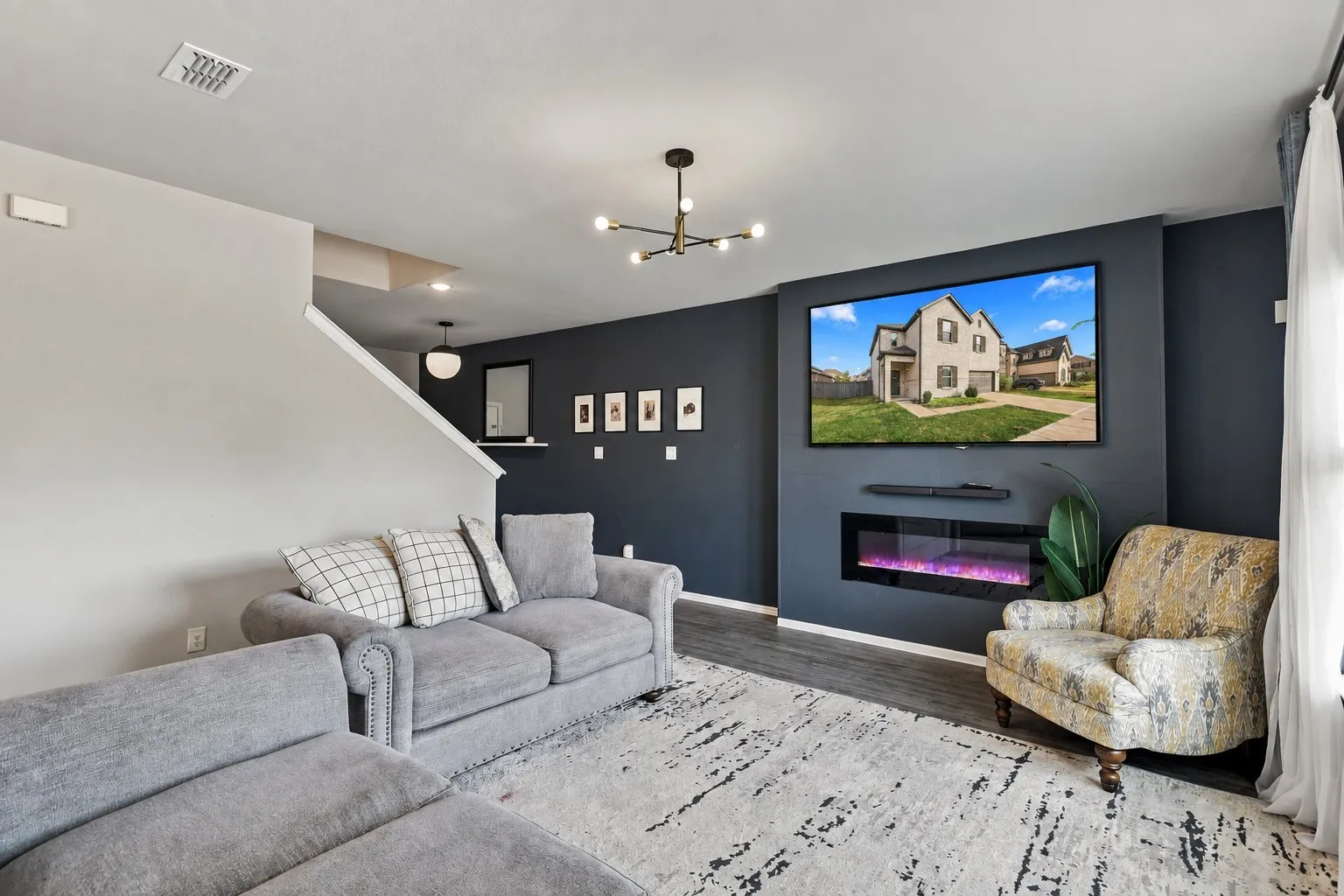 Built-in electric fireplace with a dark accent wall, wood-finish flooring, and a modern ceiling light fixture