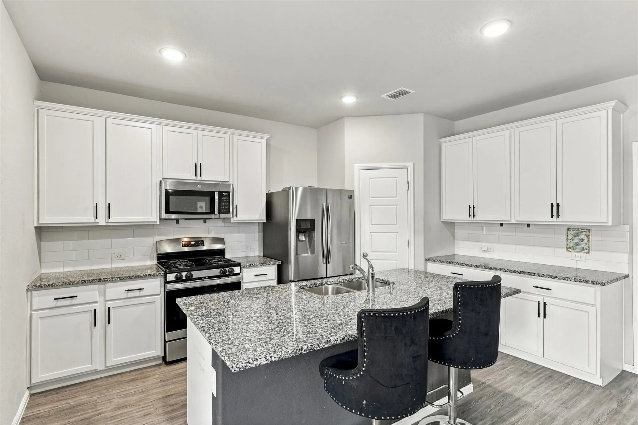 Gourmet kitchen featuring white cabinetry, stainless steel appliances, granite countertops, a tiled backsplash, and wood-finish flooring