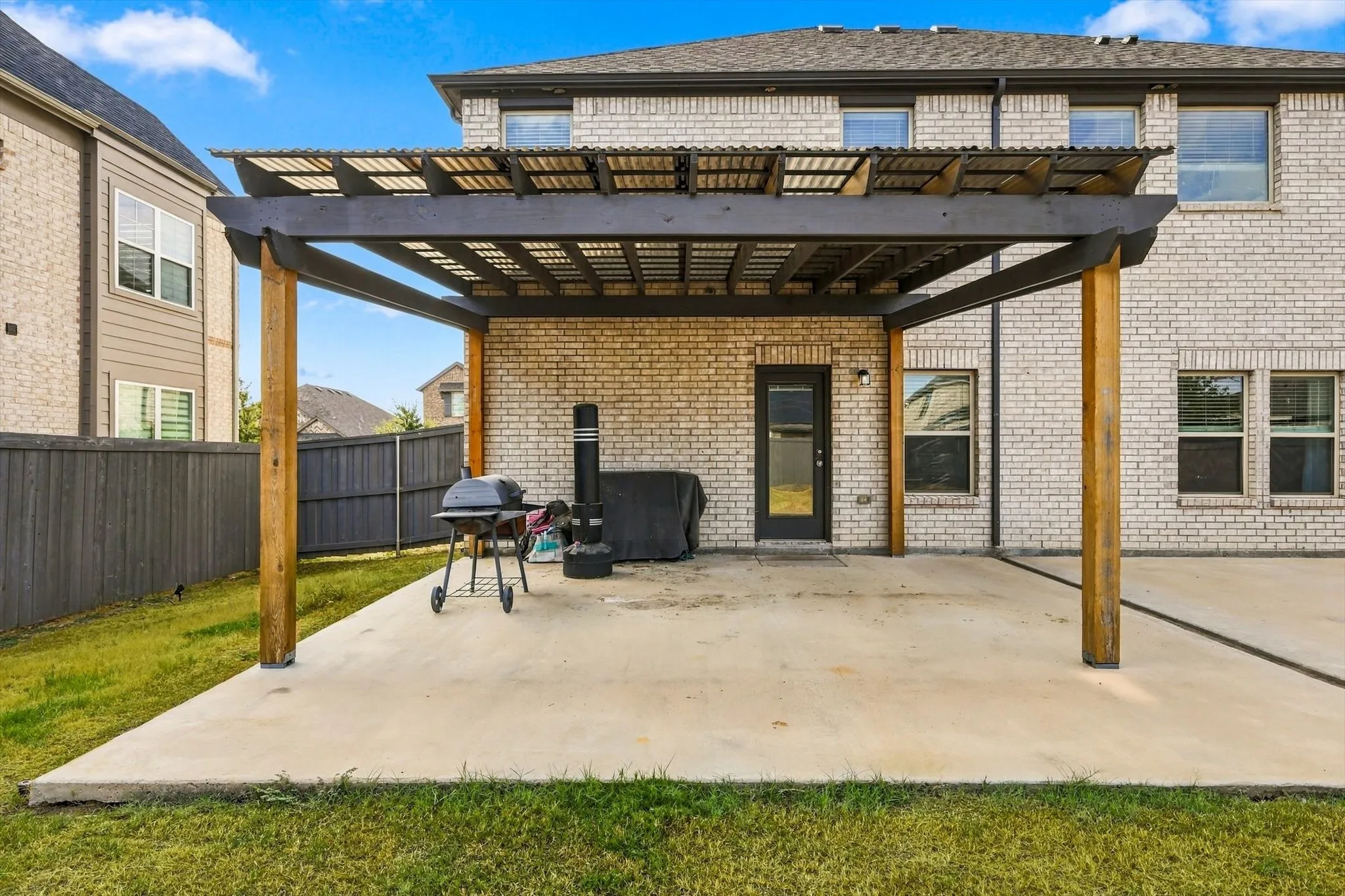 Expansive concrete patio featuring a large pergola with a slatted roof, a brick exterior, and a fenced backyard