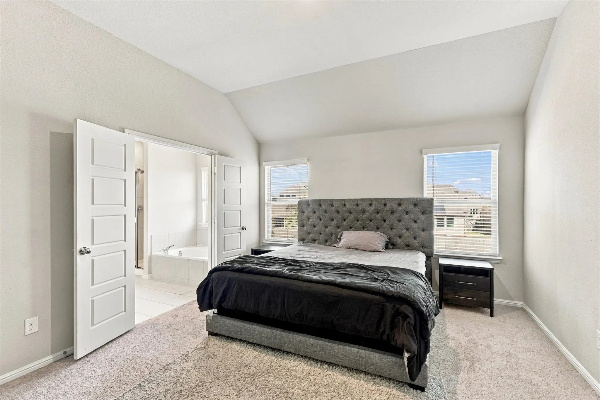 Vaulted ceiling, two windows with blinds, carpet flooring, dual panel doors, and tile flooring in the adjoining space