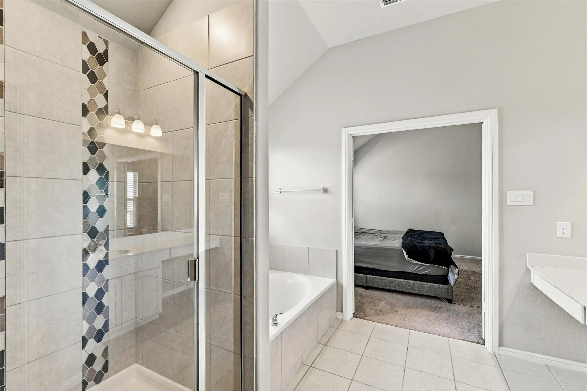 Glass-enclosed shower with decorative tile inlay, built-in soaking tub, and tile flooring