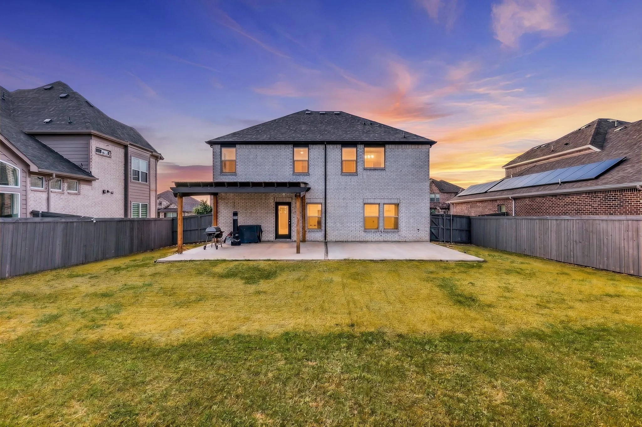 Expansive backyard featuring a manicured lawn, full privacy fencing, and a concrete patio with a wood pergola