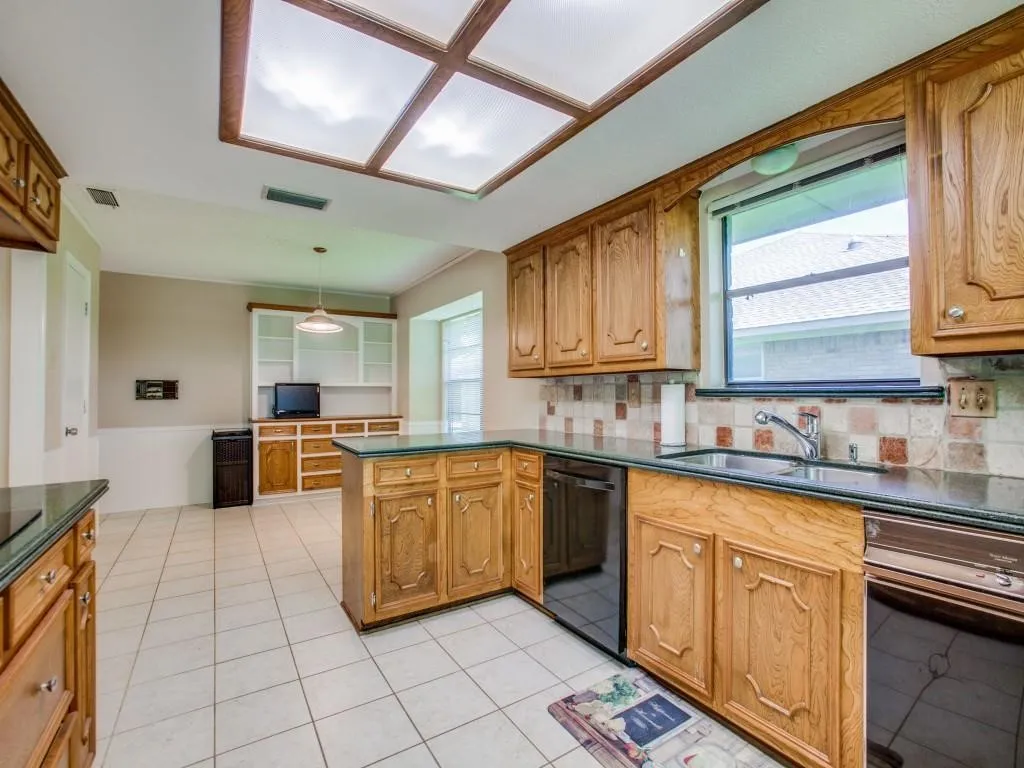 Kitchen featuring wood cabinetry, dark countertops, tiled flooring, integrated appliances, and a rectangular window