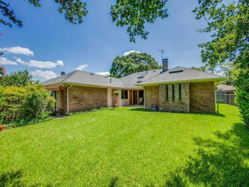 Expansive lawn area with mature landscaping, brick exterior, and a shingled roofline