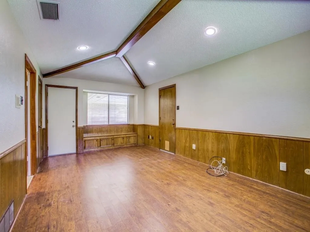 Vaulted ceiling with exposed wood beams, recessed lighting, wood-finish flooring, built-in window bench with storage, and wood paneling
