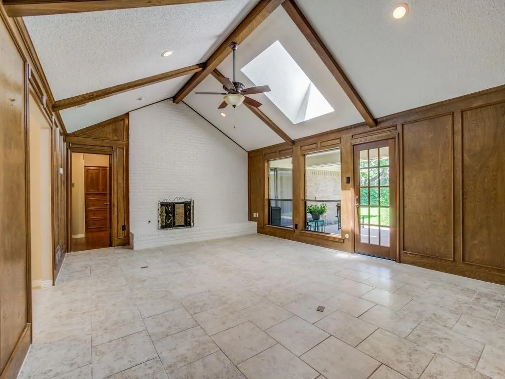 Vaulted ceiling with exposed wood beams, skylight, recessed lighting, white brick fireplace, and tile flooring