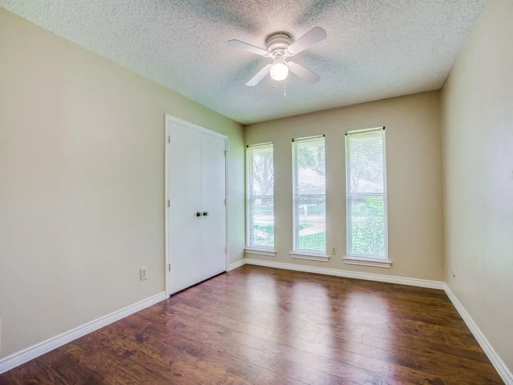 Warm wood-finish flooring, three vertical windows, and a ceiling fan with integrated lighting
