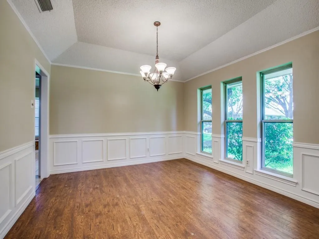Tray ceiling with crown molding, wood-finish flooring, white wainscoting, and a multi-light chandelier