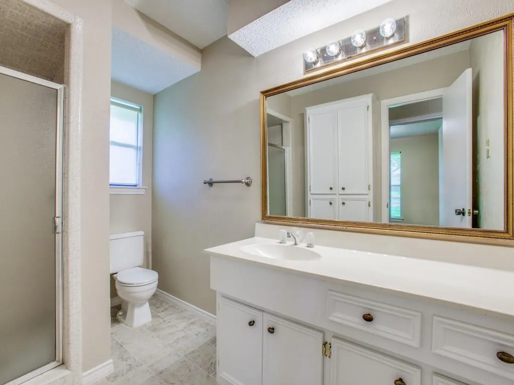 Bathroom featuring a white vanity with integrated sink, a large framed mirror, a four-light fixture, and a glass-enclosed shower
