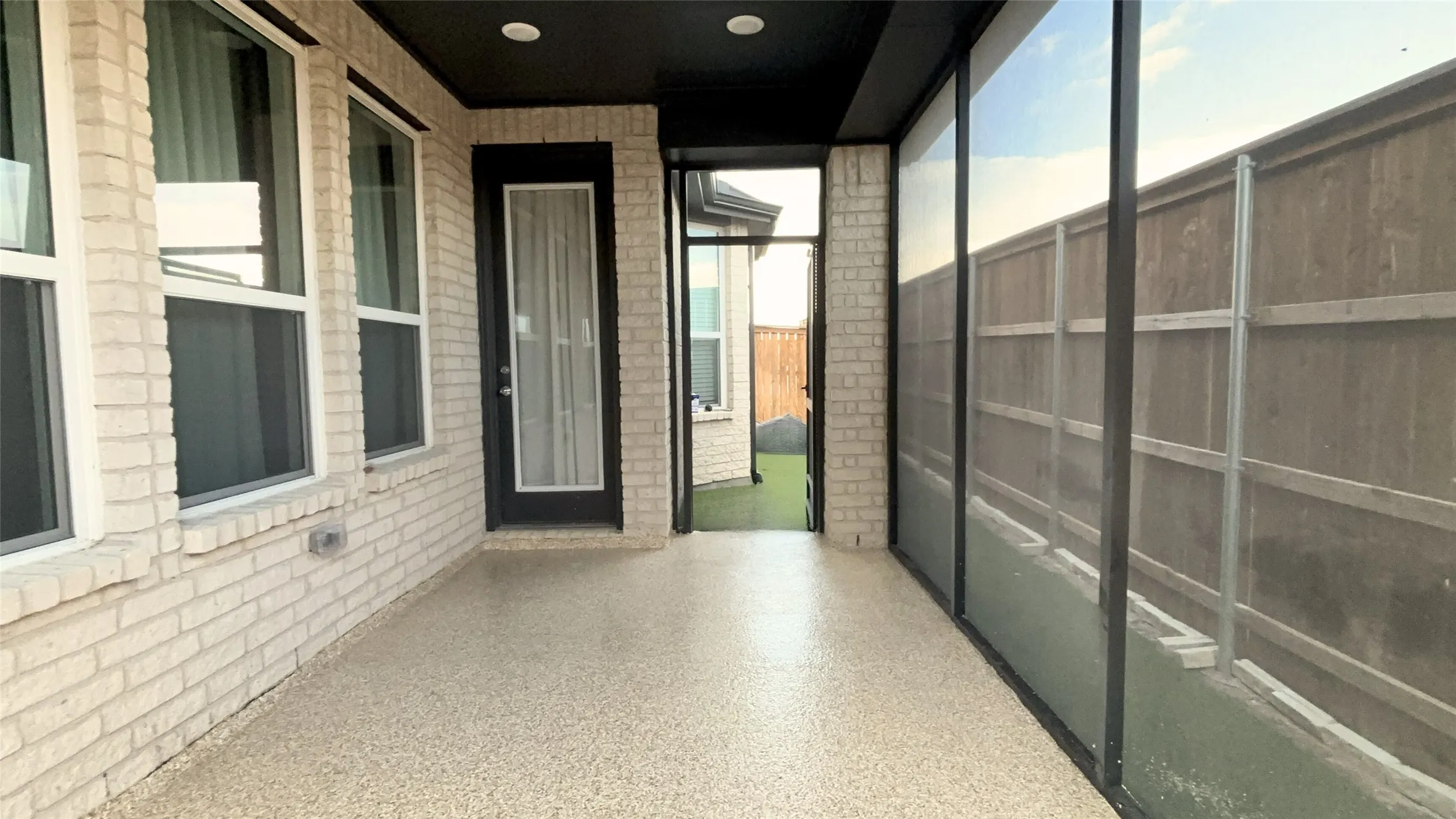 Covered patio featuring a light-colored brick exterior, a door with a full-length glass insert, and a durable textured floor coating