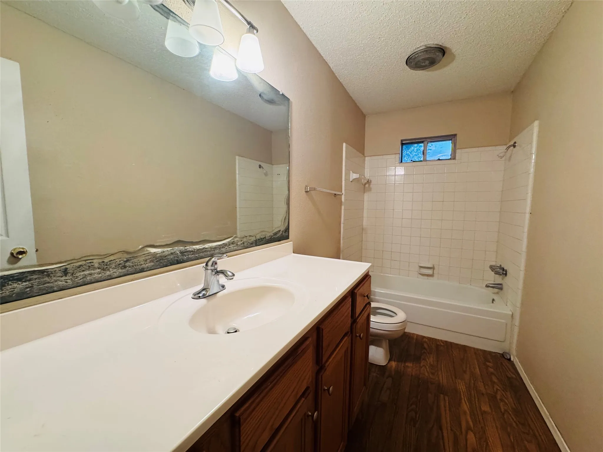 Vanity with integrated sink, wood-finish flooring, white tiled shower surround, recessed window, and wall-mounted light fixture