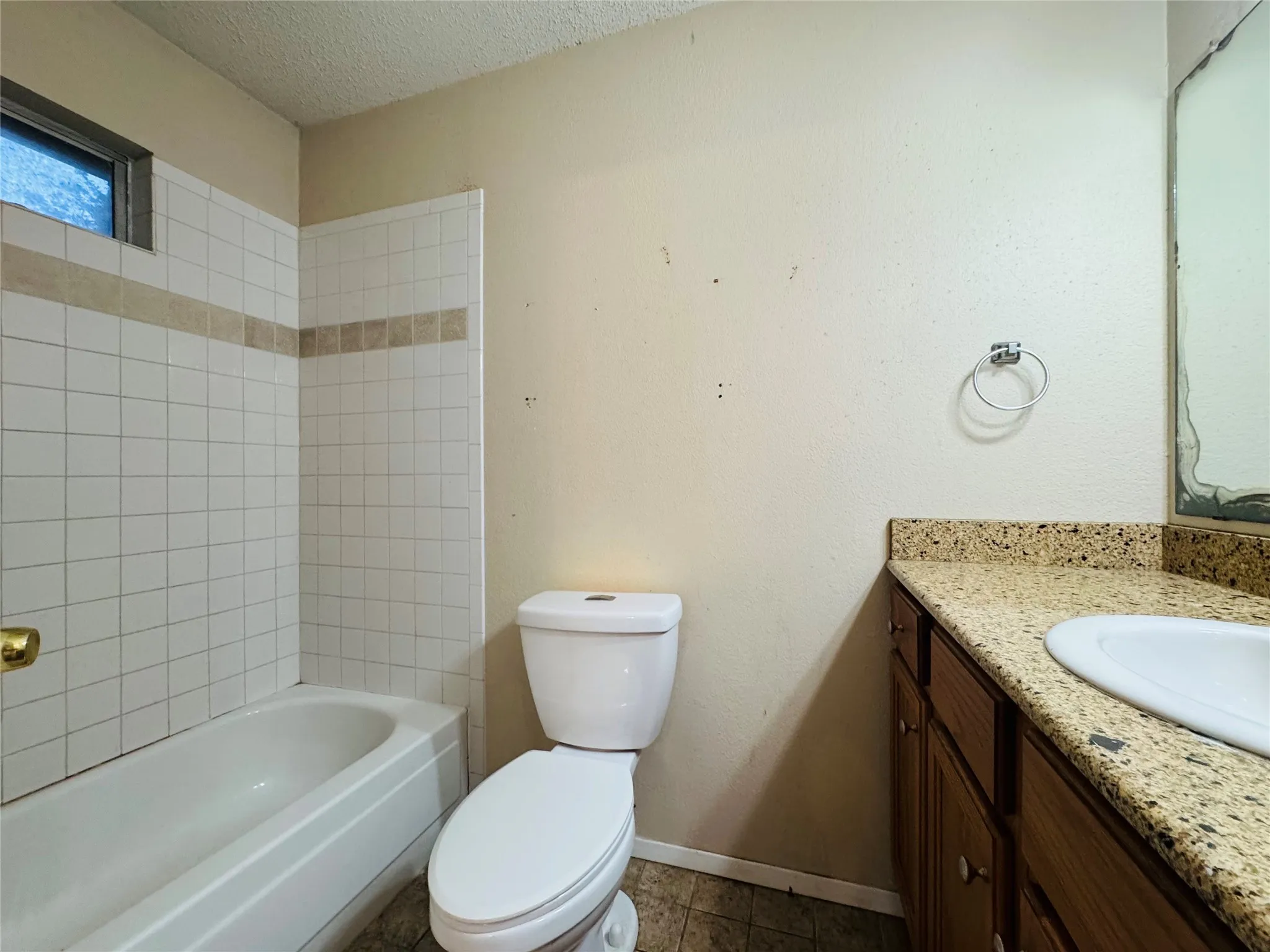 White tile tub surround with an accent band, built-in bathtub, and a vanity with a light-toned countertop and wood-finish cabinetry