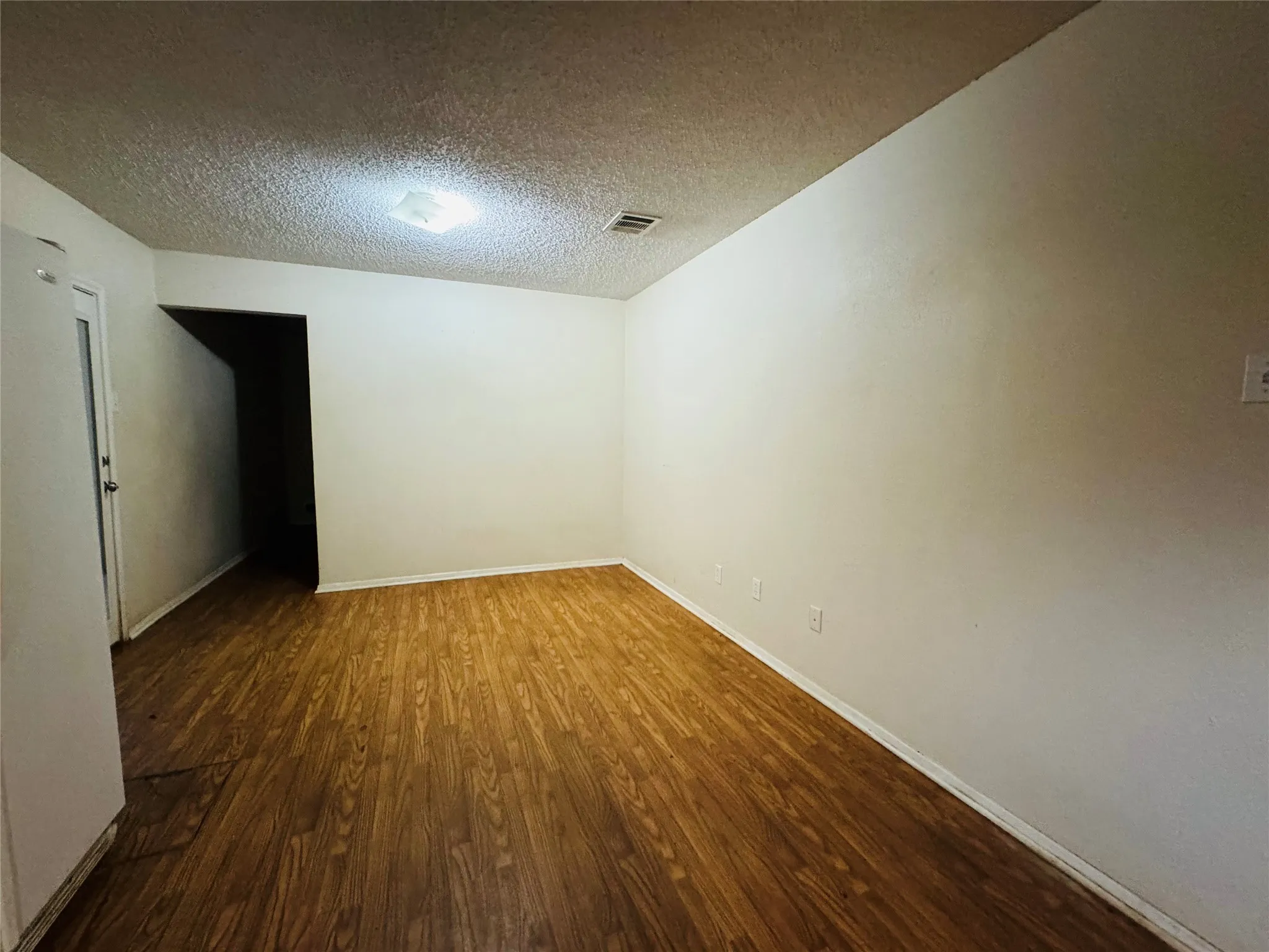 Wood-finish flooring with white baseboards, a white door, and a flush-mount ceiling light fixture