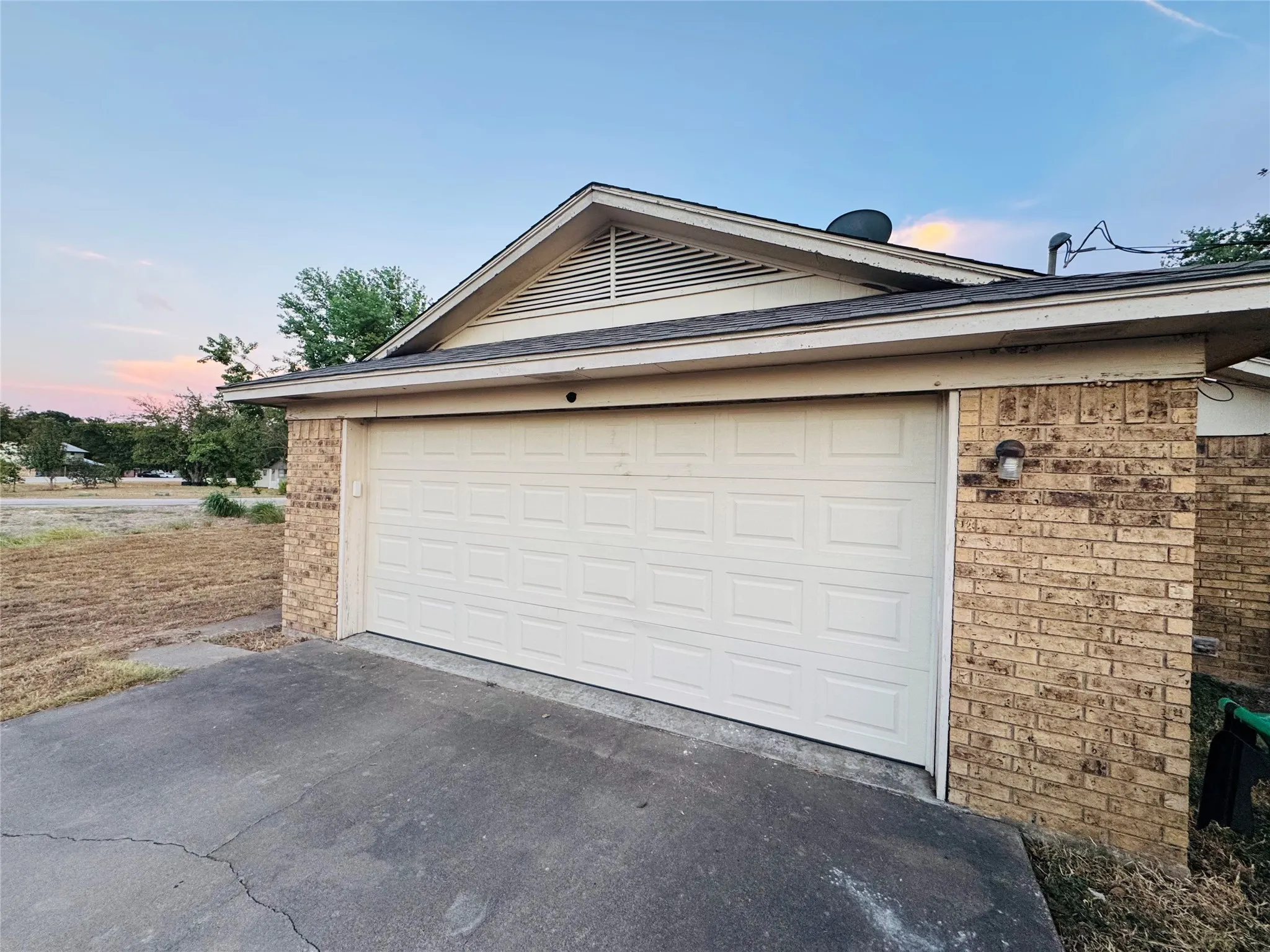 Attached garage with a panel door, brick exterior, and a gabled roofline