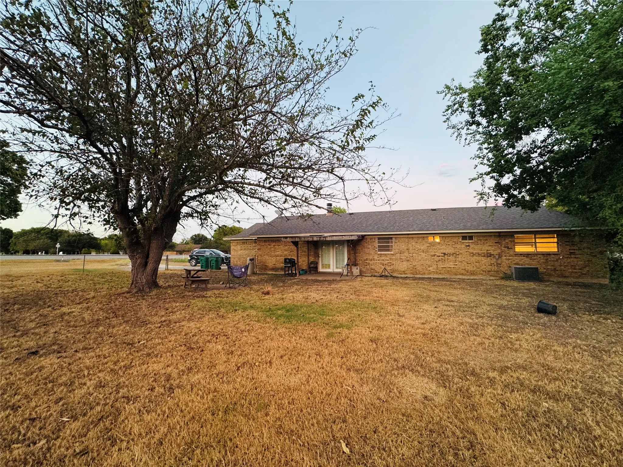 Brick exterior with a dark shingle roof, mature trees, and a spacious backyard