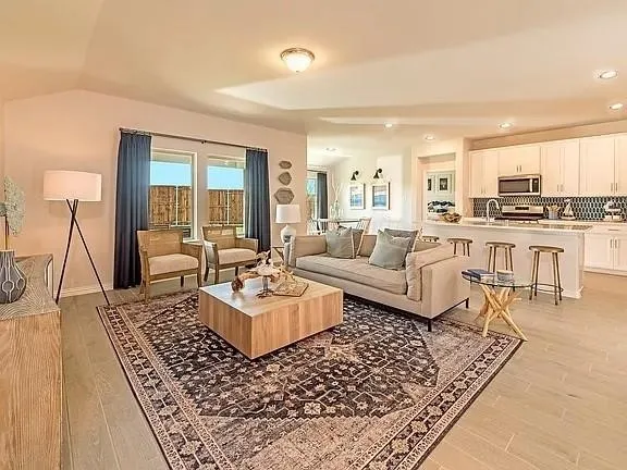 Open-concept living space featuring vaulted ceilings, wood-finish flooring, a kitchen island with seating, white shaker cabinetry, and stainless steel appliances