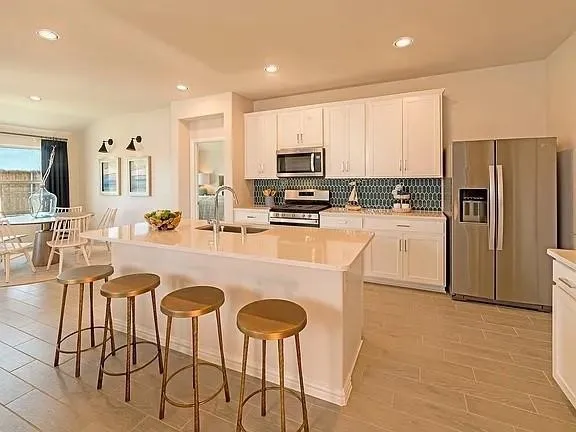 Kitchen featuring an island with a built-in sink, white cabinetry, a teal geometric tile backsplash, stainless steel appliances, and wood-finish flooring