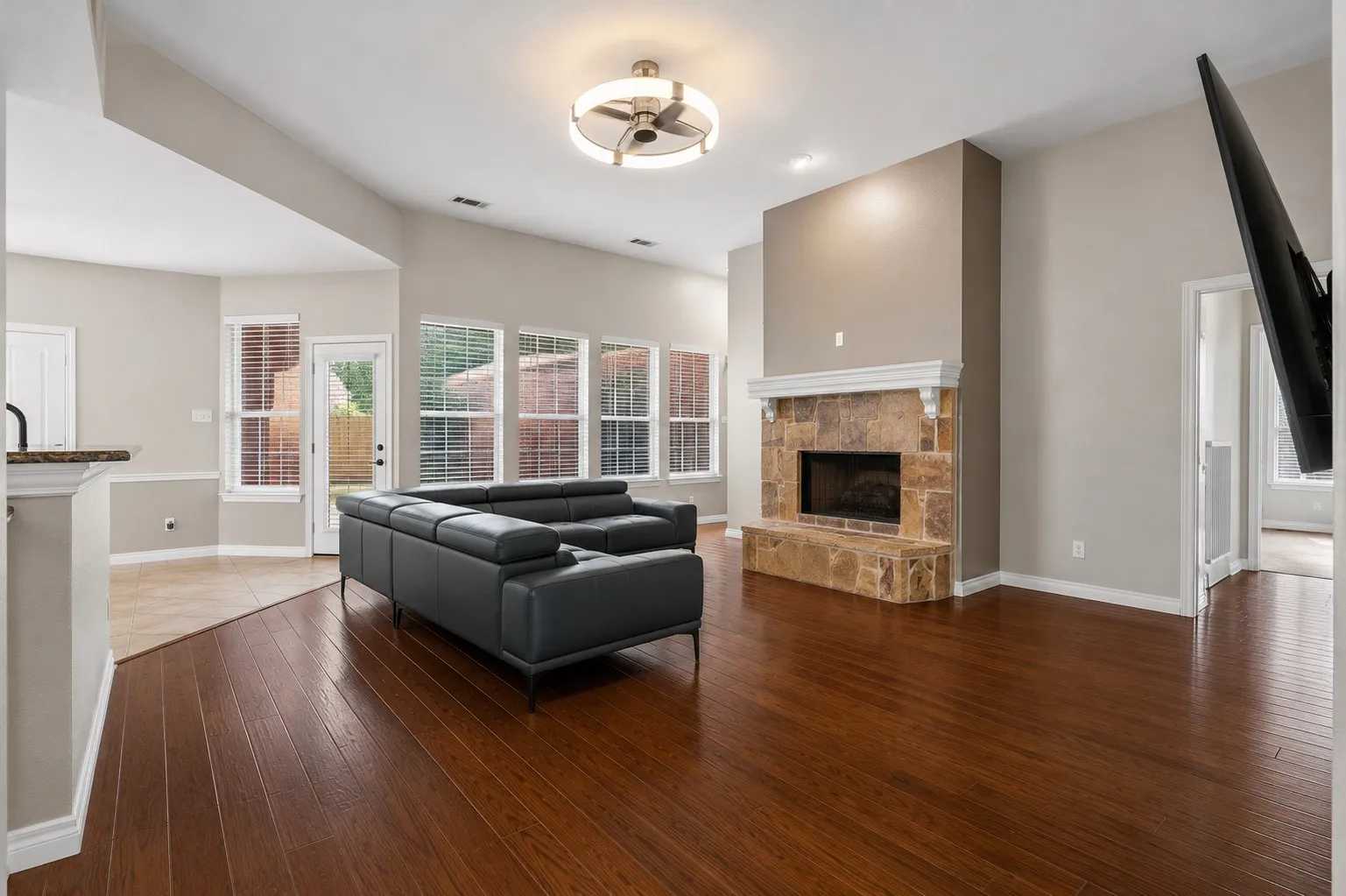Hardwood-style flooring throughout, stone-clad fireplace with mantel, recessed lighting, and a ceiling fan with integrated lighting