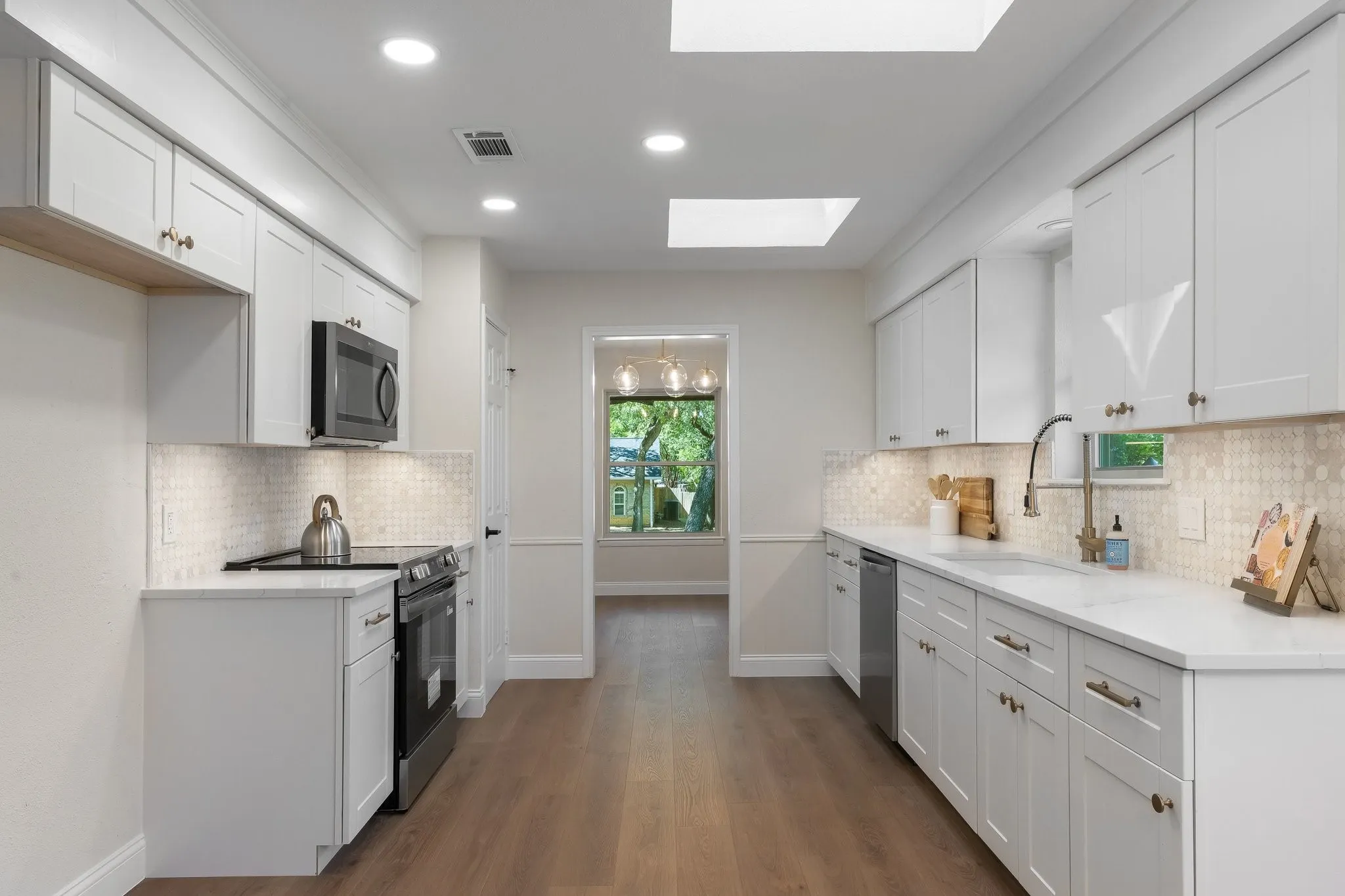 Galley kitchen featuring new white shaker cabinetry, new stainless steel appliances, recessed lighting, and a skylight