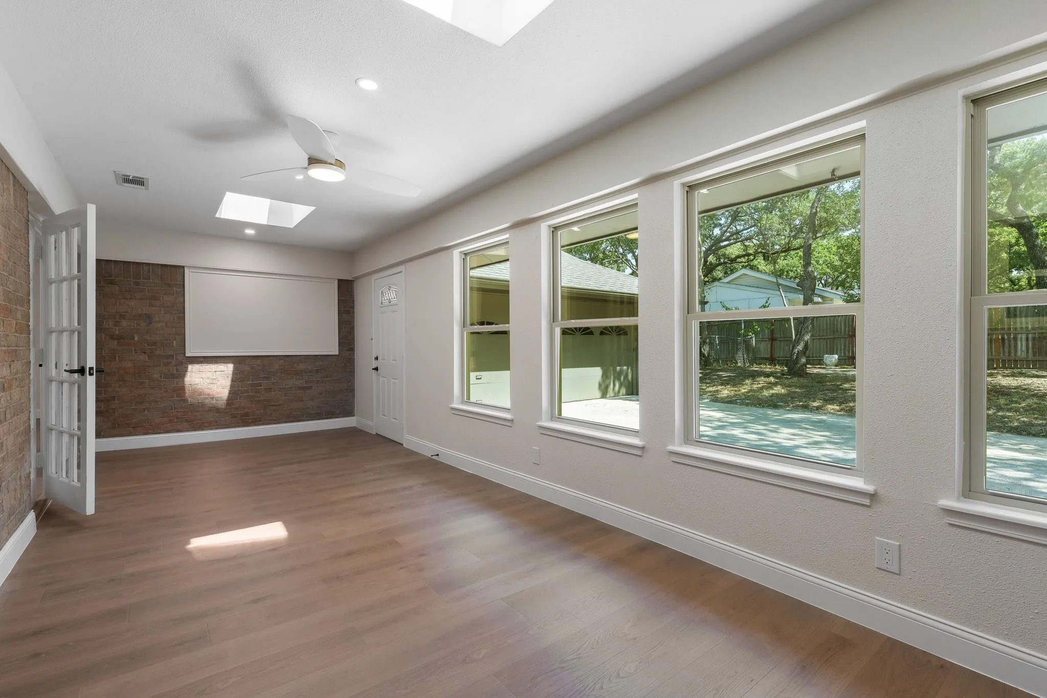 Wood-finish flooring, multiple windows, skylights, ceiling fan, and exposed brick-finish wall