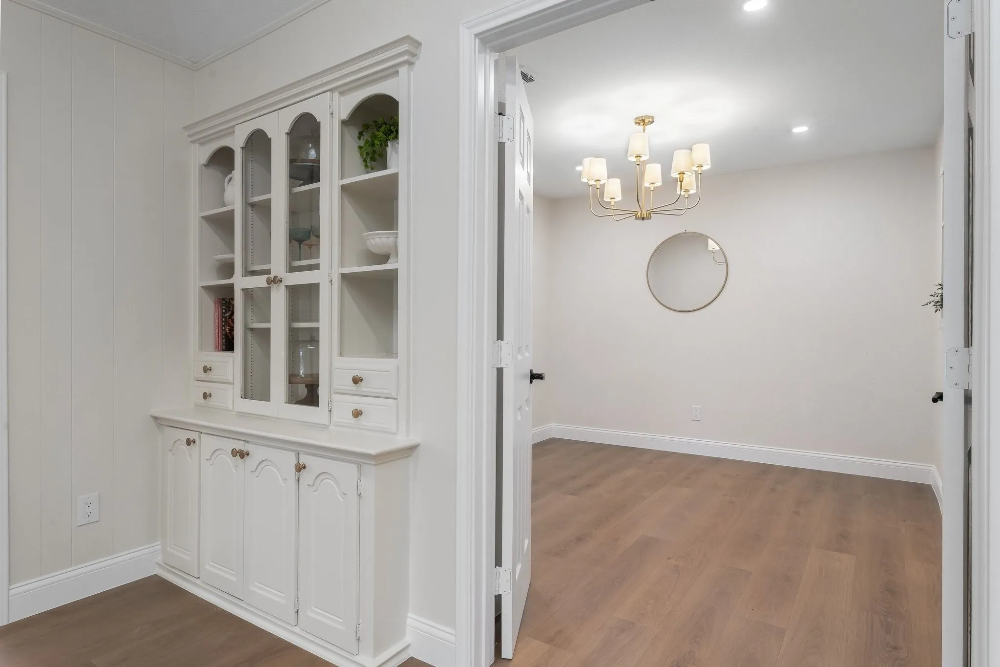 Built-in display cabinetry with glass fronts and lower storage, wood-finish flooring, recessed lighting, and a multi-arm chandelier