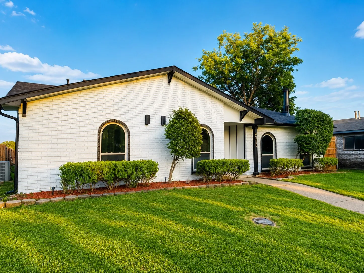White brick exterior with black trim, arched windows, and a concrete pathway