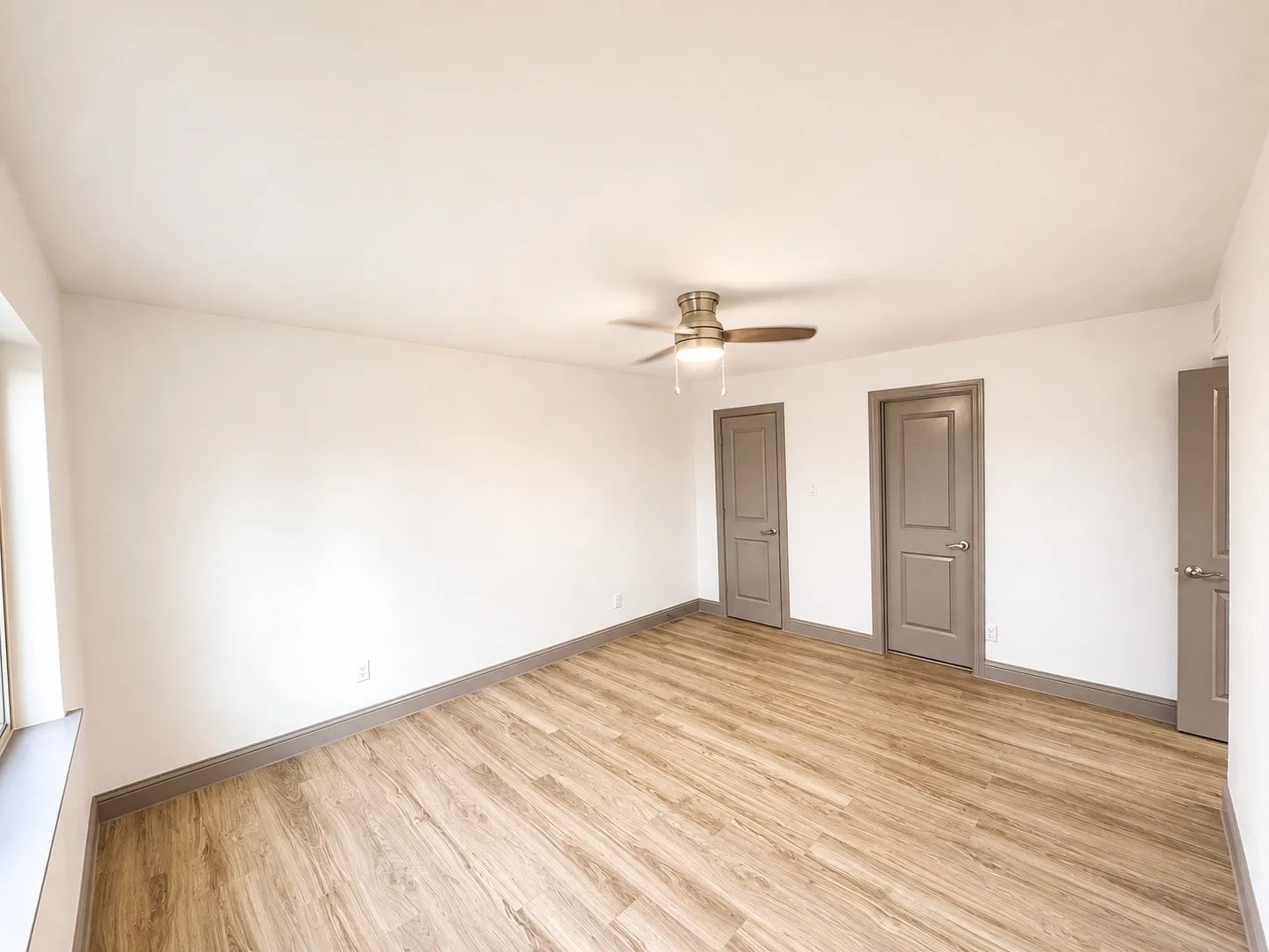 Spacious room featuring wood-finish flooring, white walls, and a ceiling fan with integrated lighting