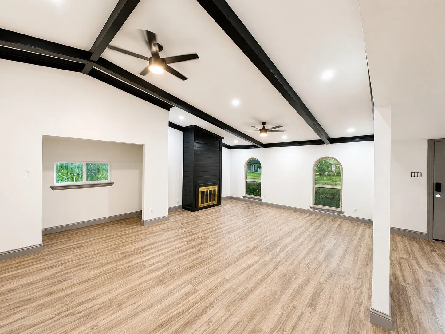 Recessed lighting throughout, wood-finish flooring, two modern ceiling fans, black accent fireplace, and two arched windows