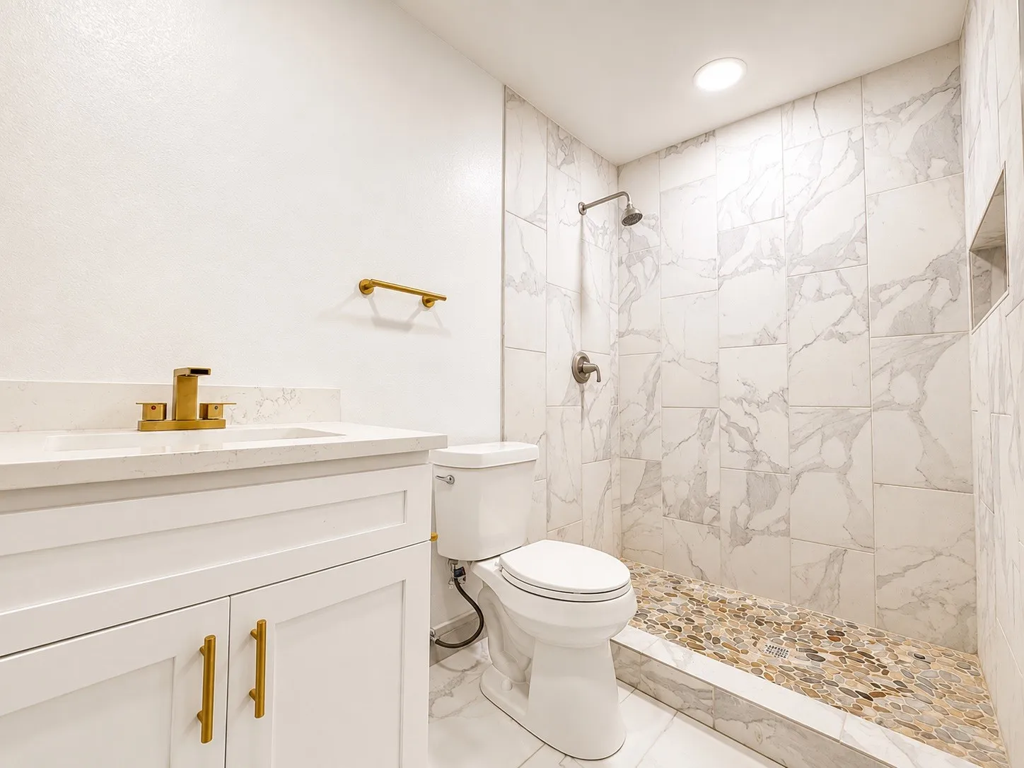 White vanity with quartz countertop, brass-finish faucet, and integrated sink