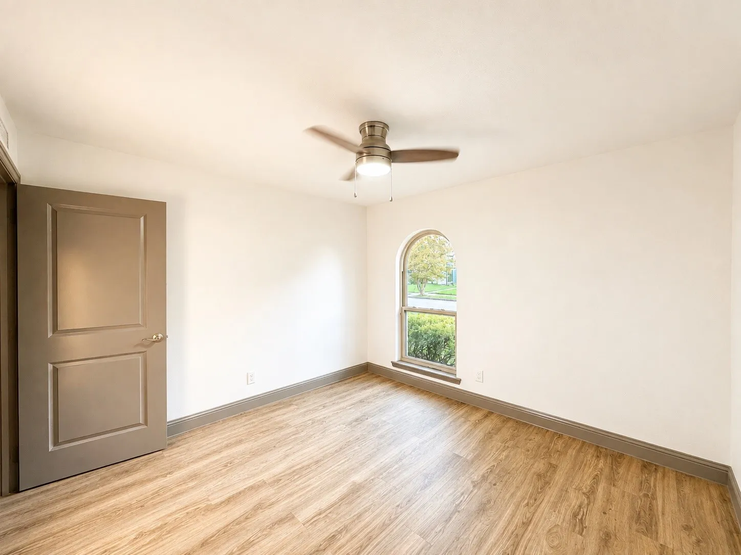 Wood-finish flooring, arched window, ceiling fan, and painted interior door