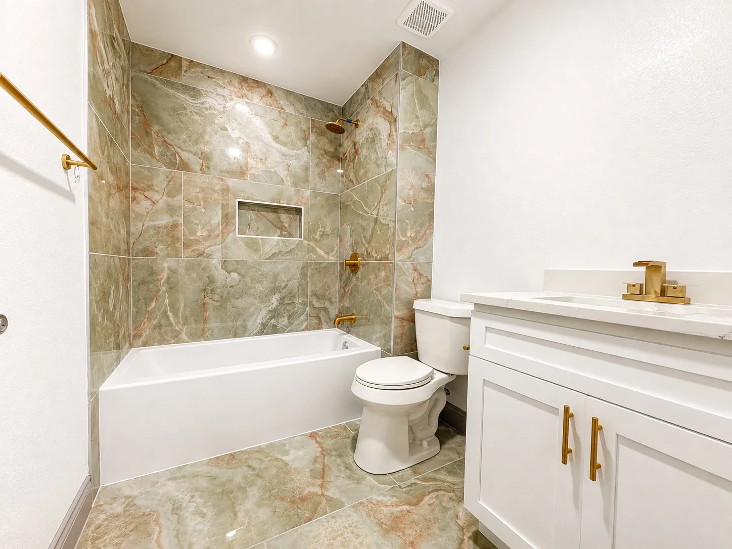 Modern bathroom featuring floor-to-ceiling green and brown marbled tile, white built-in bathtub, and a built-in shower niche