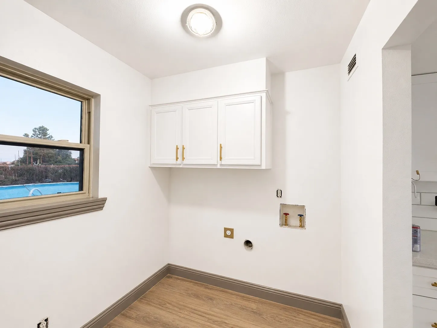 White cabinetry with gold-tone hardware, wood-finish flooring, and a single window with gray trim