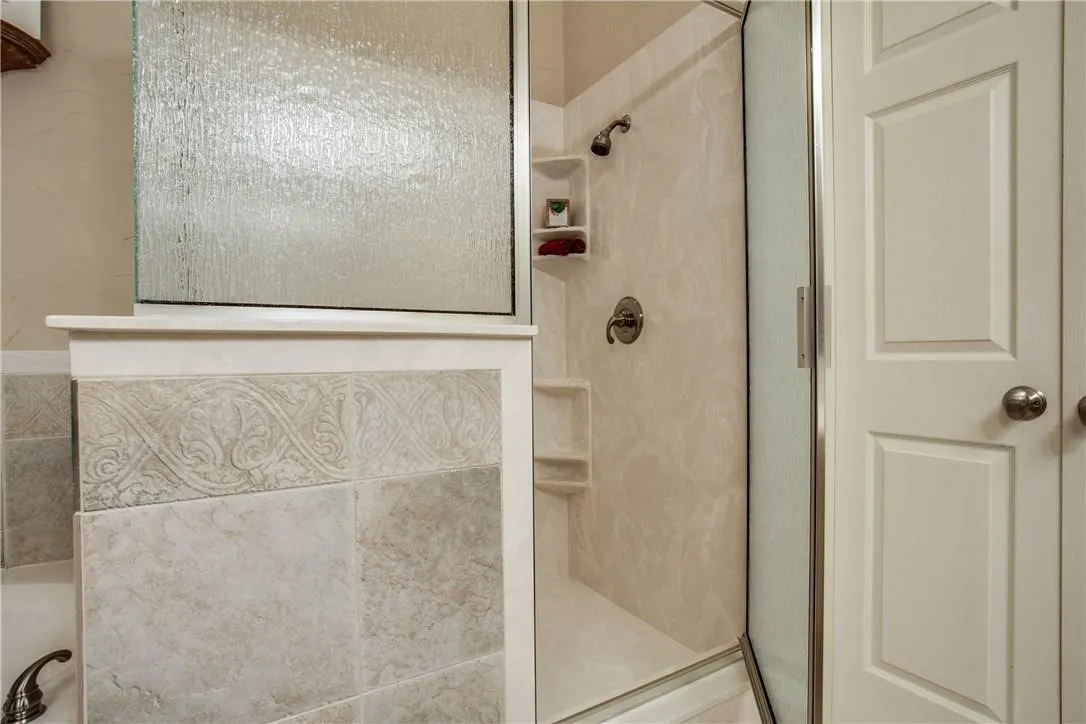 Walk-in shower with built-in shelving, glass enclosure, and decorative tiled tub surround