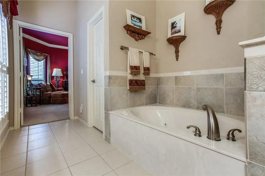 Recessed bathtub with brushed nickel fixtures, tile flooring, and wall-mounted towel bar
