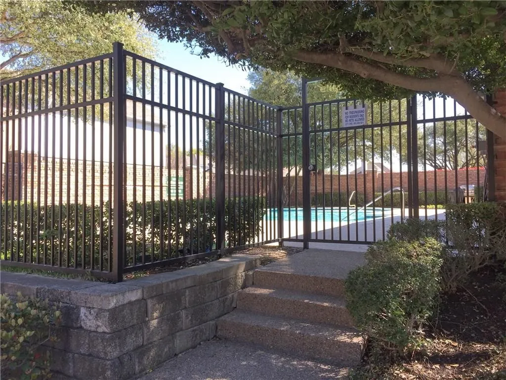 Fenced pool area featuring a black metal fence, a matching gate, concrete steps, and a retaining wall