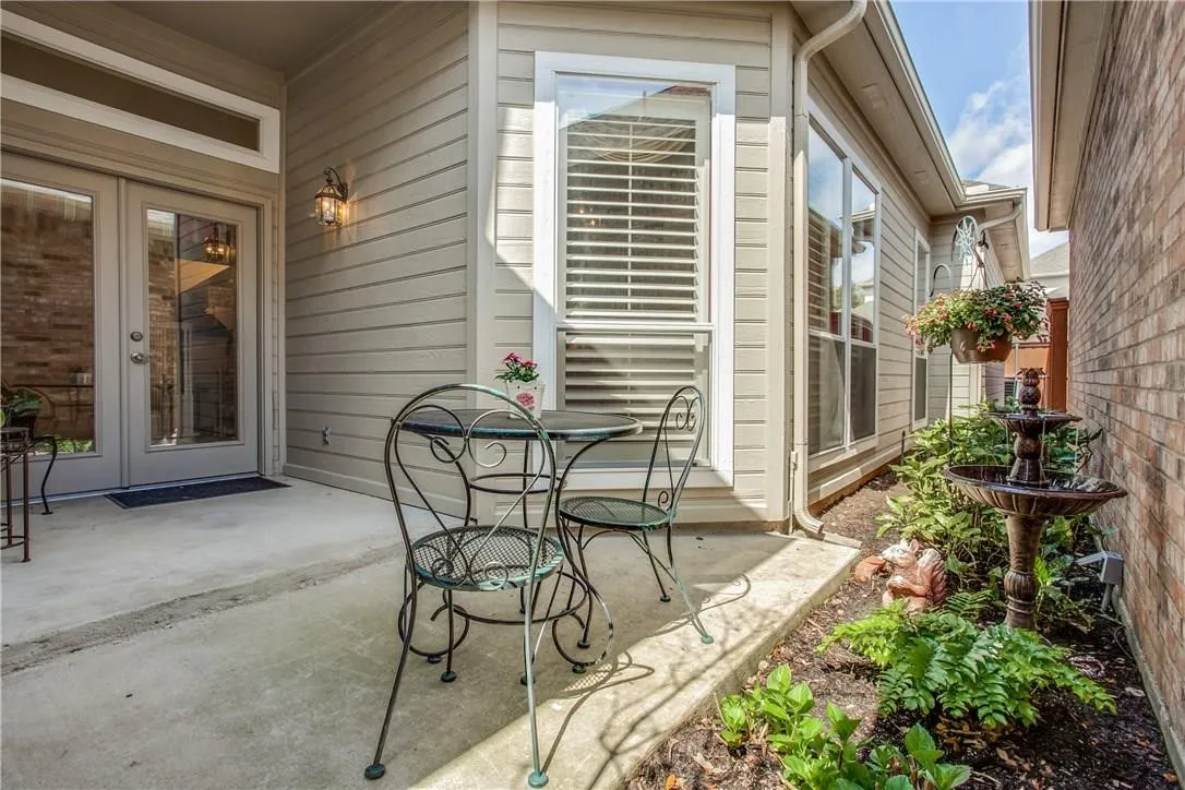 Concrete patio featuring double glass-panel doors with transom window, exterior sconce, window with blinds, and planted garden bed
