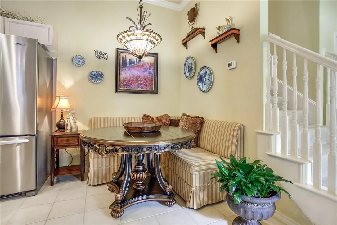 Built-in banquette seating, tile flooring, stainless steel refrigerator, white painted staircase with balusters, and an ornate chandelier
