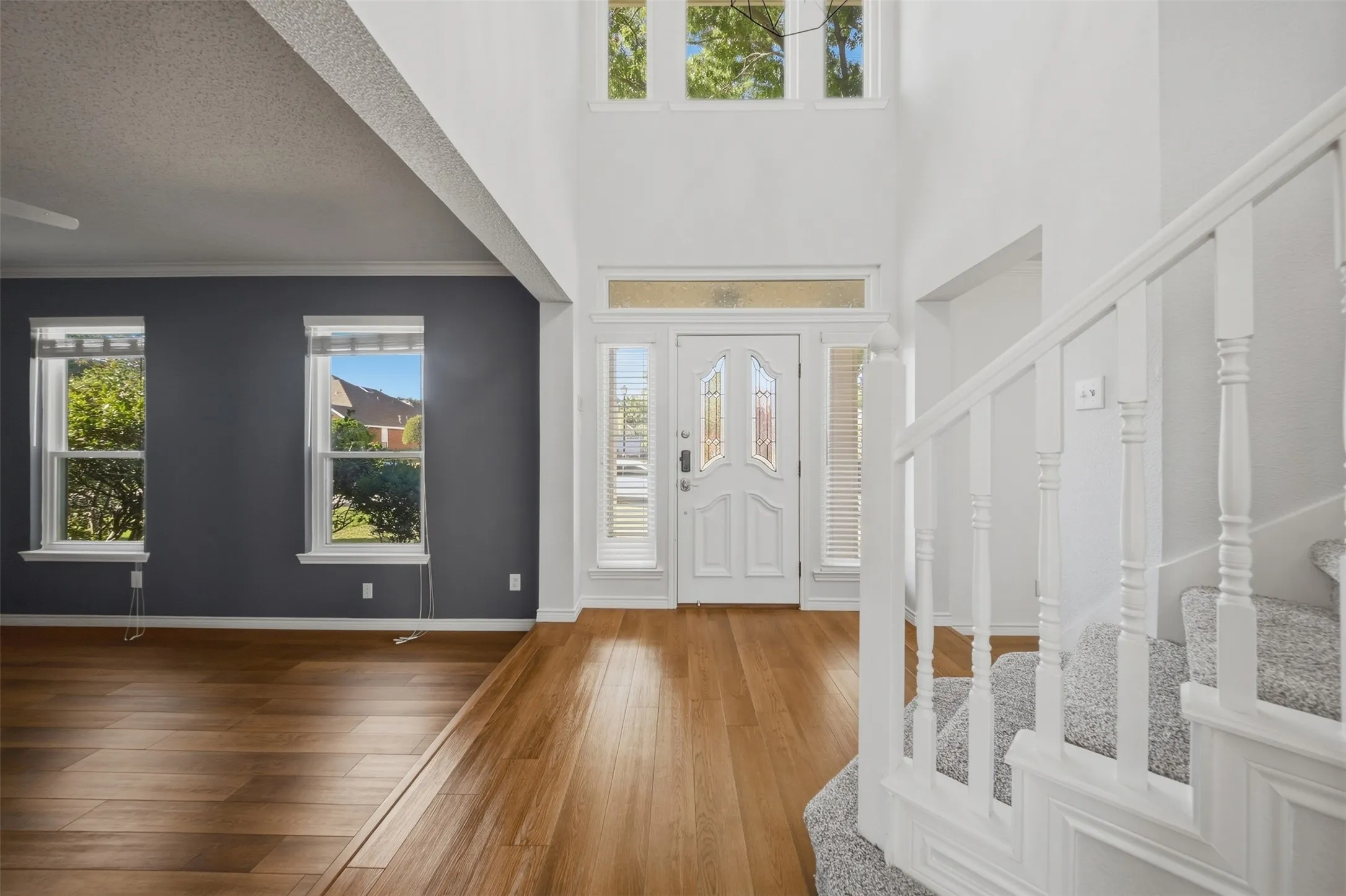 Double-height foyer with wood-finish flooring, white spindle staircase, and a white paneled entry door with decorative glass inserts