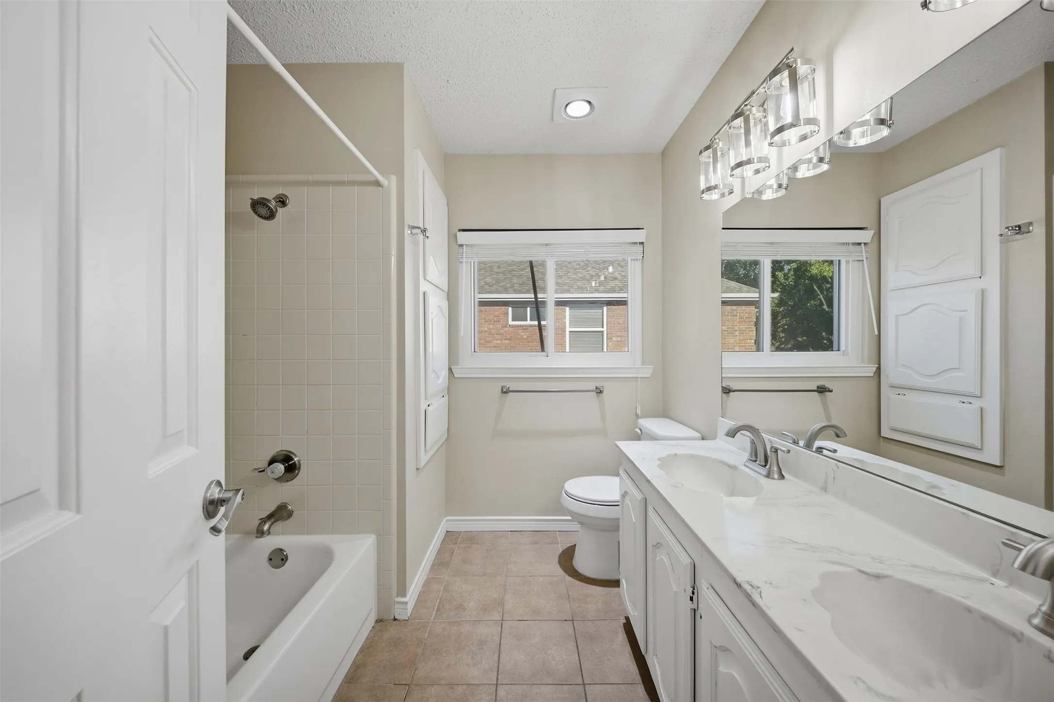 Dual vanity with undermount sinks, tile flooring, built-in storage cabinetry, tub with shower, and double windows