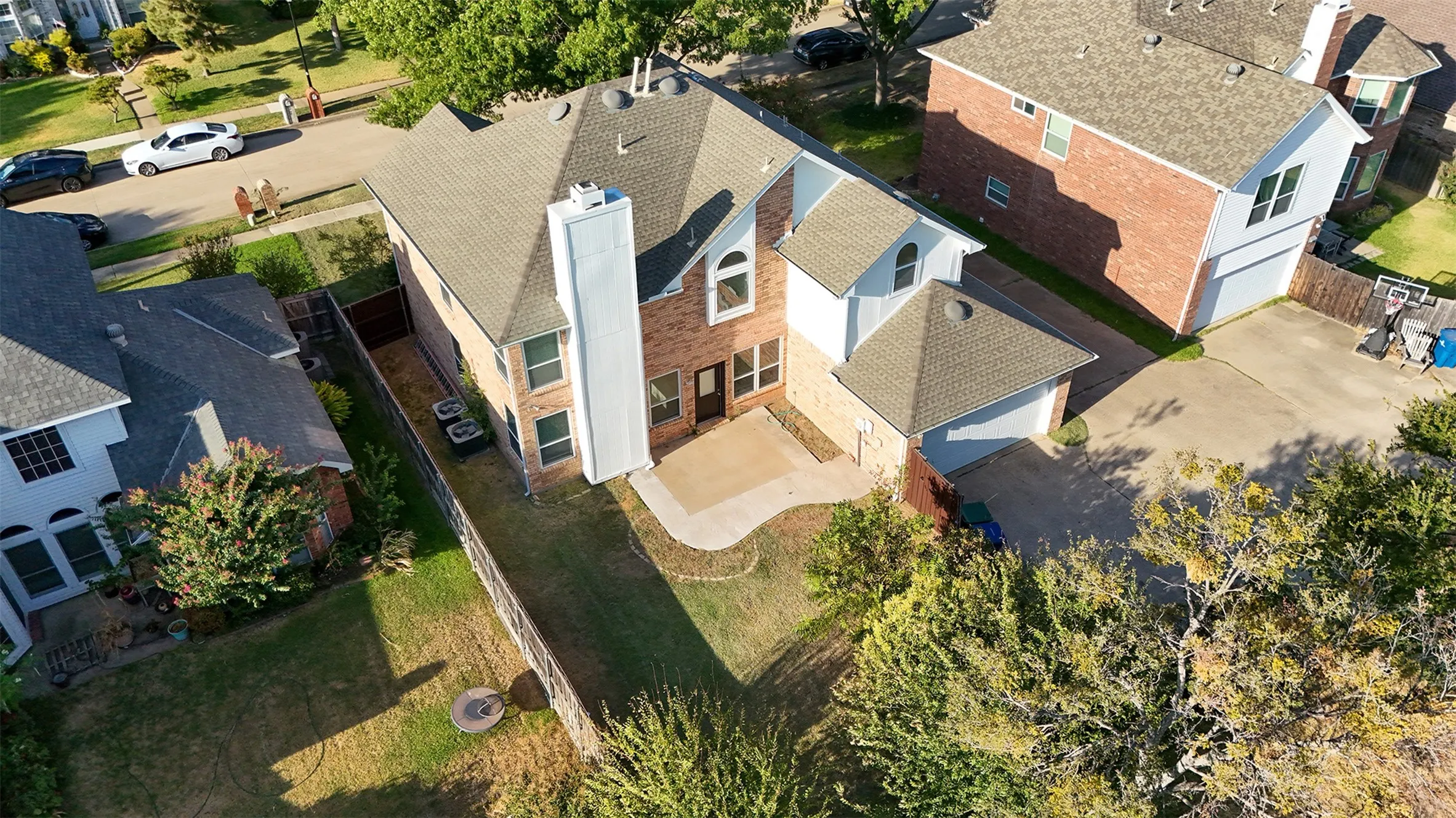 Brick and siding exterior with a multi-level roofline, attached garage, concrete patio, and a fenced backyard