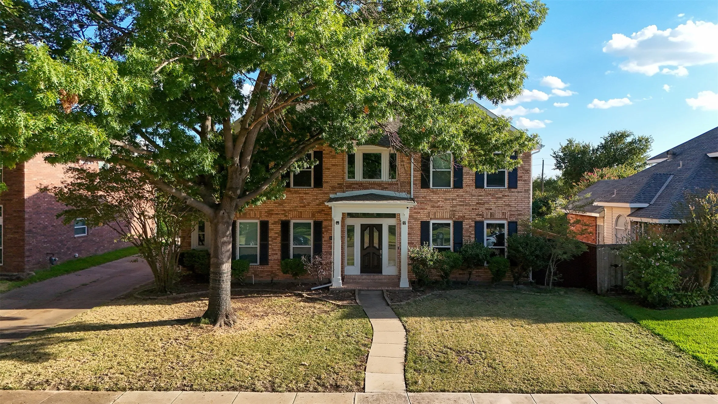 Two-story brick facade residence featuring a covered entry, dark shutters, and a mature tree